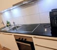 Modern kitchen with white cabinets, black countertops, stainless steel sink, induction cooktop, oven, and coffee machine.