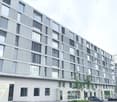 Modern multi-story building with grey facade, large windows, and balconies. Features contemporary design with clean lines and a mix of glass and concrete elements.