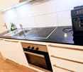 Modern kitchen with white cabinets, black countertops, stainless steel sink, induction cooktop, oven, and coffee machine.