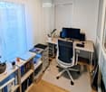 A well-organized home office with a desk, ergonomic chair, laptop, monitor, and various storage items including books and plants.