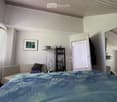 Cozy bedroom with a large bed, sofa, floor lamp, shelf, and mirror. The room features white walls, a window with blinds, and a picture frame on the wall.