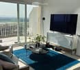 Modern living room with large windows offering a scenic view, a sofa with pillows, a coffee table, a TV stand, a floor lamp, and a small plant.