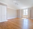 Empty room with wooden flooring, white walls, large window, and white door.