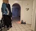 Hallway with tiled floor, arched doorway leading to another room, coats and bags hanging on the wall, small decorative item on the wall.