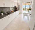 Modern kitchen with white cabinets, marble backsplash, stainless steel sink, and a dining area with a table and chairs. Offers a scenic view through large windows.