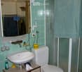 Bathroom with green tiled walls, a white sink, a toilet, a shower with a glass enclosure, and a mirror above the sink. The sink has a faucet, and there are various toiletries and a towel visible.
