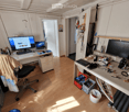 A well-lit room with wooden flooring, two desks, a chair, and various electronic equipment and tools.