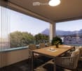 Balcony with a wooden table, chairs, a potted plant, and a cup, overlooking a scenic mountain view.