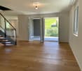 Bright, empty hallway with wooden flooring, modern staircase, and large sliding doors leading to a balcony with a scenic view.