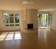 Bright, unfurnished living room with wooden flooring, large windows, fireplace, and sliding glass doors leading to a balcony.