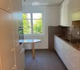 Modern kitchen with white cabinets, dark tiled floor, and a small round wooden table near the window.
