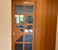 A modern wooden door with glass panels is set into a light-colored wall, featuring a sleek design with a visible handle and a small decorative element on the glass.