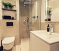 Modern bathroom with a toilet, sink, shower, and a large mirror. Features include a glass-enclosed shower, a sleek sink with a modern faucet, and decorative plants on a shelf.