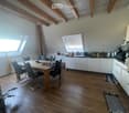 Open-plan kitchen and dining area with wooden beams, white cabinets, and a dining table with chairs.