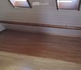 Completely empty room with wooden flooring and white paneled walls. Two skylights provide natural light.