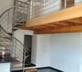Open-plan space with a modern spiral staircase leading to an upper level, featuring a countertop, cabinet, and stool.