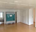 Empty room with wooden flooring, white walls, and a large green cabinet with a decorative tile front. The room has several doors and a window letting in natural light.