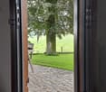 View from inside through a large window or door onto a stone-paved patio area leading to a grassy lawn and trees.