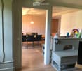 A well-lit hallway leads to a dining area with a table and chairs, and a small sitting area with a stool and decorative items.
