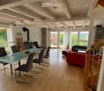 Bright, open-plan living and dining area with wooden floors, large windows, a red sofa, a glass dining table with chairs, and a fireplace.