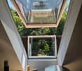 Loft-style room with skylight windows, wooden floor, round metallic table, speaker, and storage box.