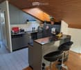 Modern kitchen with grey cabinets, stainless steel appliances, a central island with bar stools, and a skylight above.