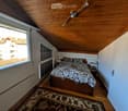 Cozy attic bedroom with wooden ceiling, large window offering a view, bed with patterned bedding, nightstand, and a patterned rug.