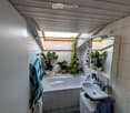 Bathroom with a bathtub, sink, mirror, cabinet, and toilet. Features a skylight window, potted plants, and a towel hanging on the wall.