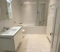 modern bathroom with white tiles, bathtub, shower, toilet, sink, mirror, and radiator