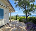 A stone pathway leads to a house with a view of a lake and mountains, surrounded by lush greenery and lavender plants.