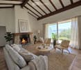 Living room with exposed wooden beams, fireplace, sofa, coffee table, and large windows offering a scenic view.