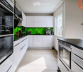Modern kitchen with white cabinets, stainless steel appliances, and a green backsplash. Features an oven, fridge, sink, and coffee machine.
