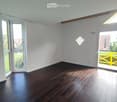Empty room with wooden flooring, white walls, large windows, and a sliding door leading to a balcony.