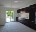 Modern kitchen with dark cabinets, white countertops, and a large window overlooking a garden.