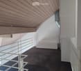 Modern hallway with wooden slatted ceiling, white walls, dark concrete floor, and white metal railings leading to an open area.