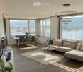 modern living room with large windows, wooden floor, dining table, couch, coffee table, TV, plants