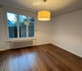 Empty room with wooden flooring, large windows, radiator, and a hanging light fixture.