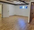 Empty room with wooden flooring, white walls, and two doors leading to adjacent spaces. A small window is visible on one wall.