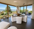 Modern living room with large windows offering scenic views, featuring white furniture including sofas, chairs, a round table, and decorative candle holders.