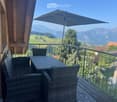 Balcony with wicker furniture, umbrella, and scenic mountain view.