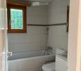Modern bathroom with a bathtub, toilet, sink, and showerhead. Grey tiled walls and wooden ceiling.