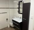 Modern bathroom with a white sink, dark wooden cabinet, mirror, toilet, and tiled walls.