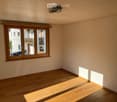 Empty room with wooden flooring and large windows, allowing natural light to fill the space.