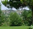 A scenic view of a village nestled in a lush green valley, surrounded by trees and hills, with houses and a church visible in the distance.