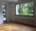 Empty room with wooden flooring, large windows, radiator, and glass door leading to outdoor area.