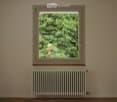 Empty room with wooden flooring, a window showing greenery outside, and a radiator below the window.