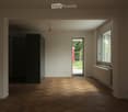 Empty room with wooden herringbone flooring, white walls, and large windows allowing natural light. A radiator is visible under one window, and a doorway leads to an outdoor area.
