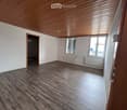Empty room with wooden flooring, white walls, and a wooden ceiling. Features a door leading to another room and windows with blinds.