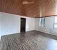 Empty room with wooden flooring, white walls, and a wooden slanted ceiling. Features a window with shutters and a doorway leading to another space.