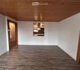 Empty room with wooden flooring and white walls, featuring a wooden ceiling and two open doors leading to other rooms.